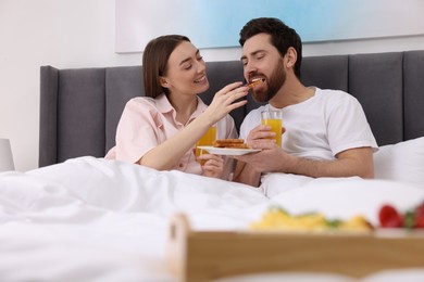 Photo of Tasty breakfast. Happy wife feeding her husband in bed at home