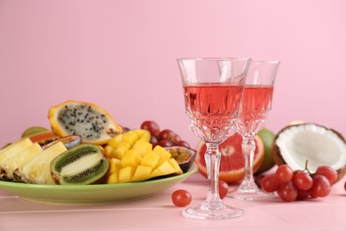 Delicious exotic fruits and glasses of wine on pink wooden table