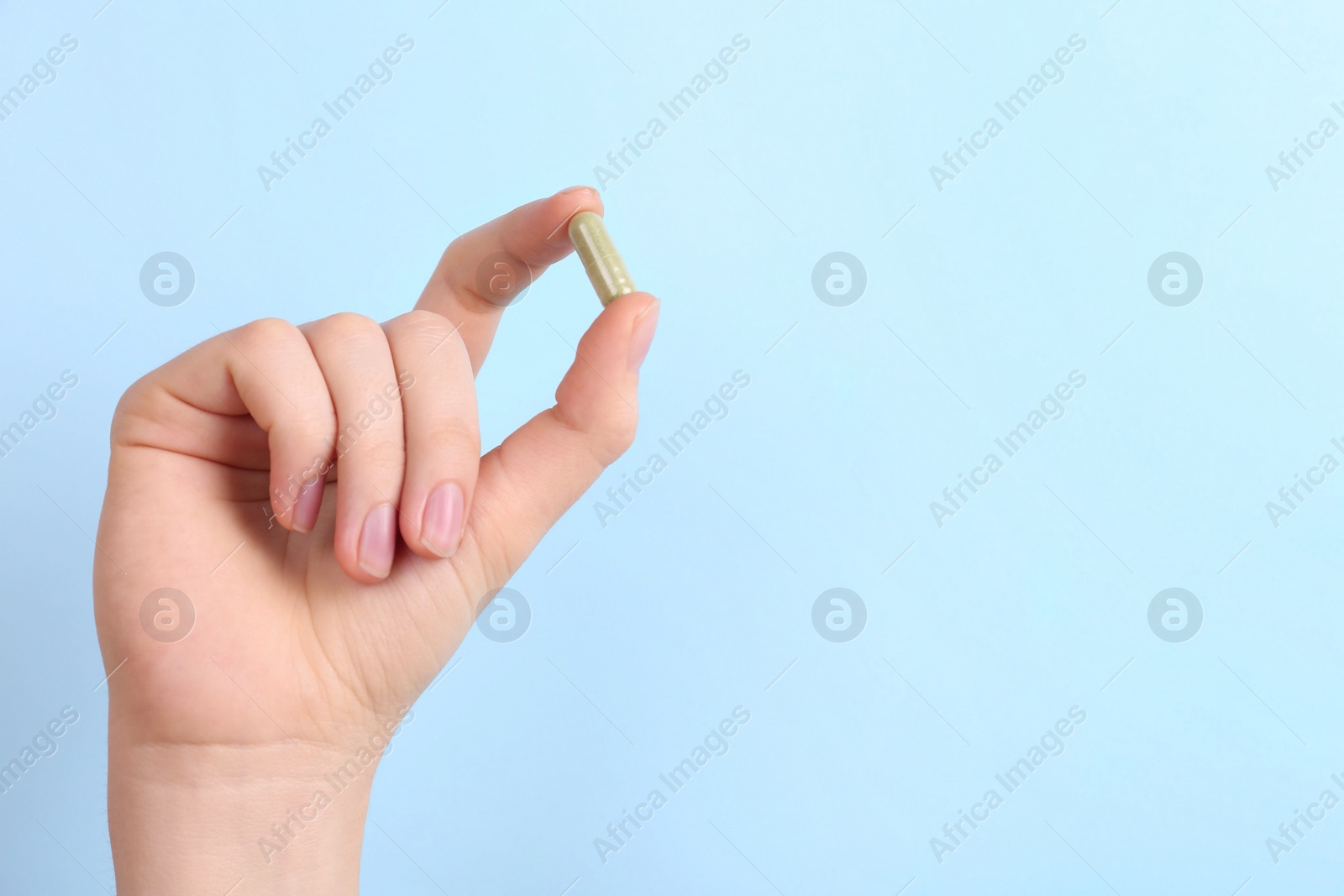 Photo of Woman holding vitamin capsule on light blue background, closeup. Space for text