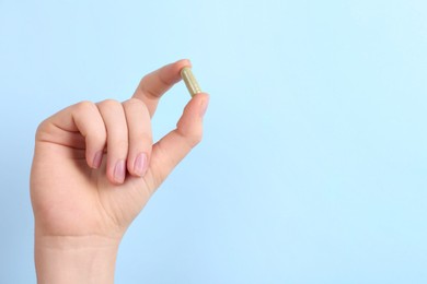 Woman holding vitamin capsule on light blue background, closeup. Space for text