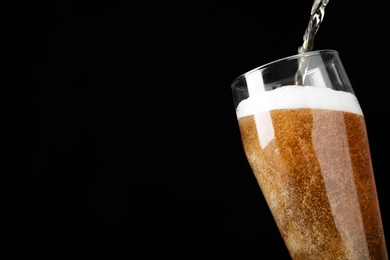 Photo of Pouring cold tasty beer into glass on black background, closeup. Space for text