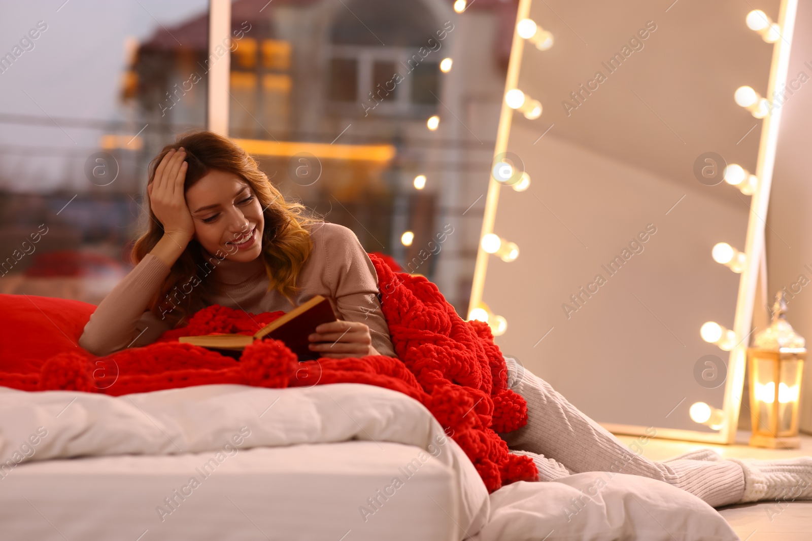 Photo of Beautiful young woman with book relaxing on bed at home. Cozy atmosphere