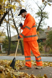 Street cleaner sweeping fallen leaves outdoors on autumn day