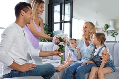 Photo of Happy family with little children congratulating mature woman in living room