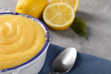 Photo of Delicious lemon curd in bowl, fresh citrus fruits and spoon on grey table, closeup