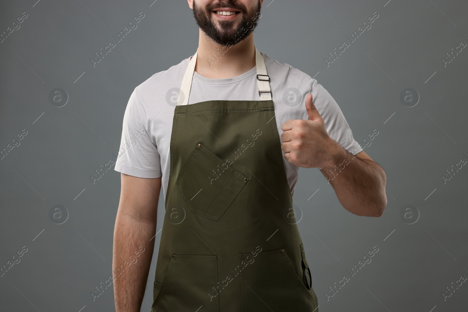 Photo of Smiling man in kitchen apron showing thumb up on grey background, closeup. Mockup for design