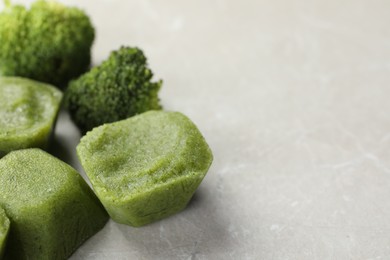 Photo of Frozen broccoli puree cubes with ingredient on marble table, closeup. Space for text