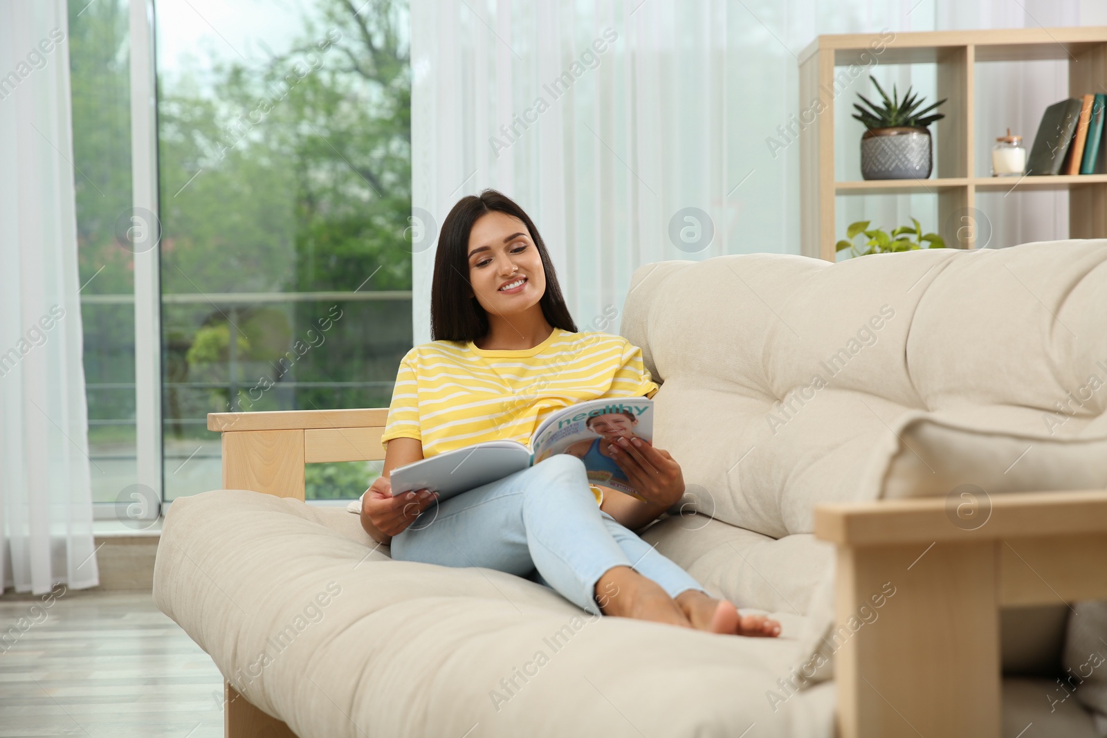 Photo of Young woman reading magazine on sofa at home