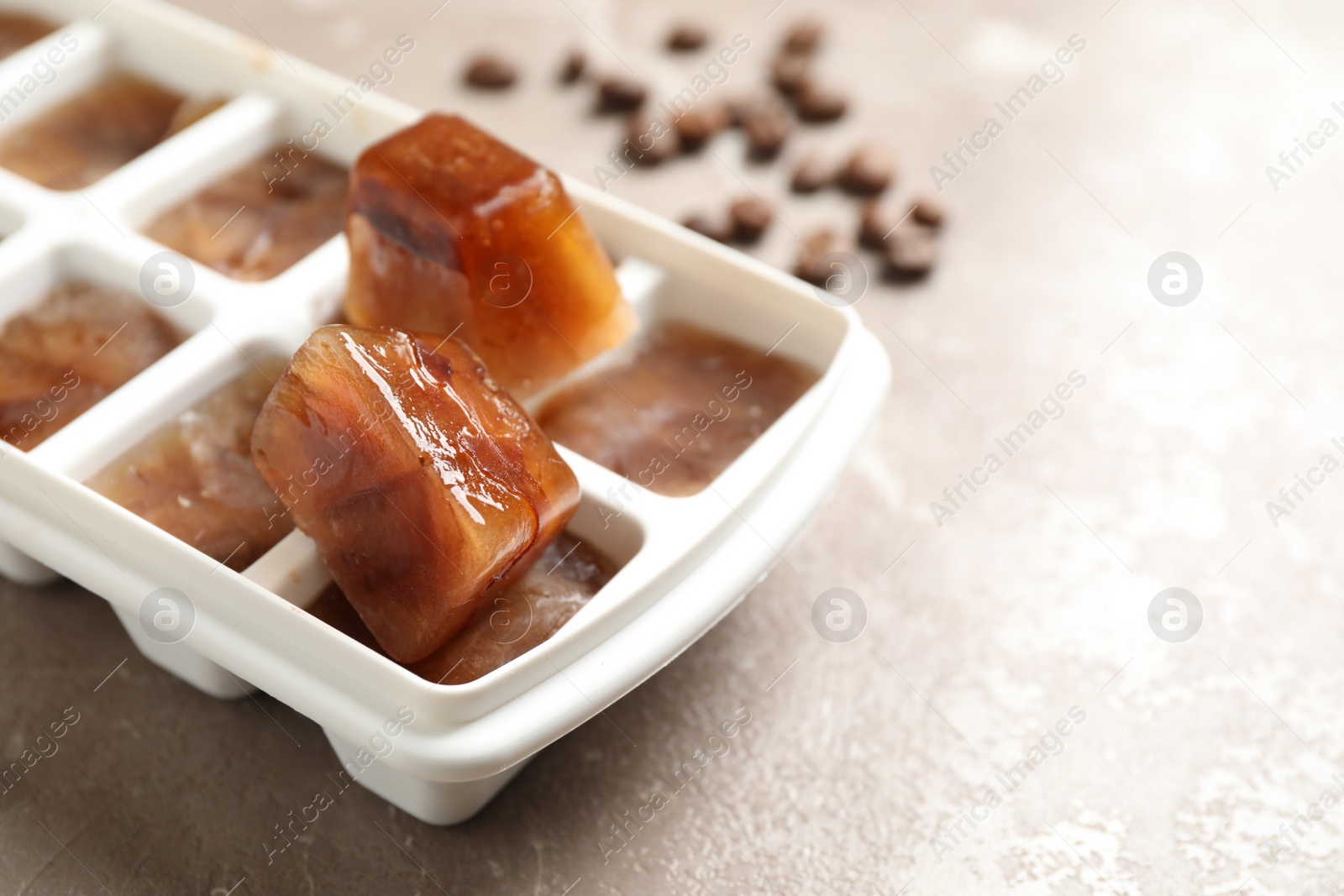 Photo of Ice cube tray with frozen coffee on grey table, closeup. Space for text