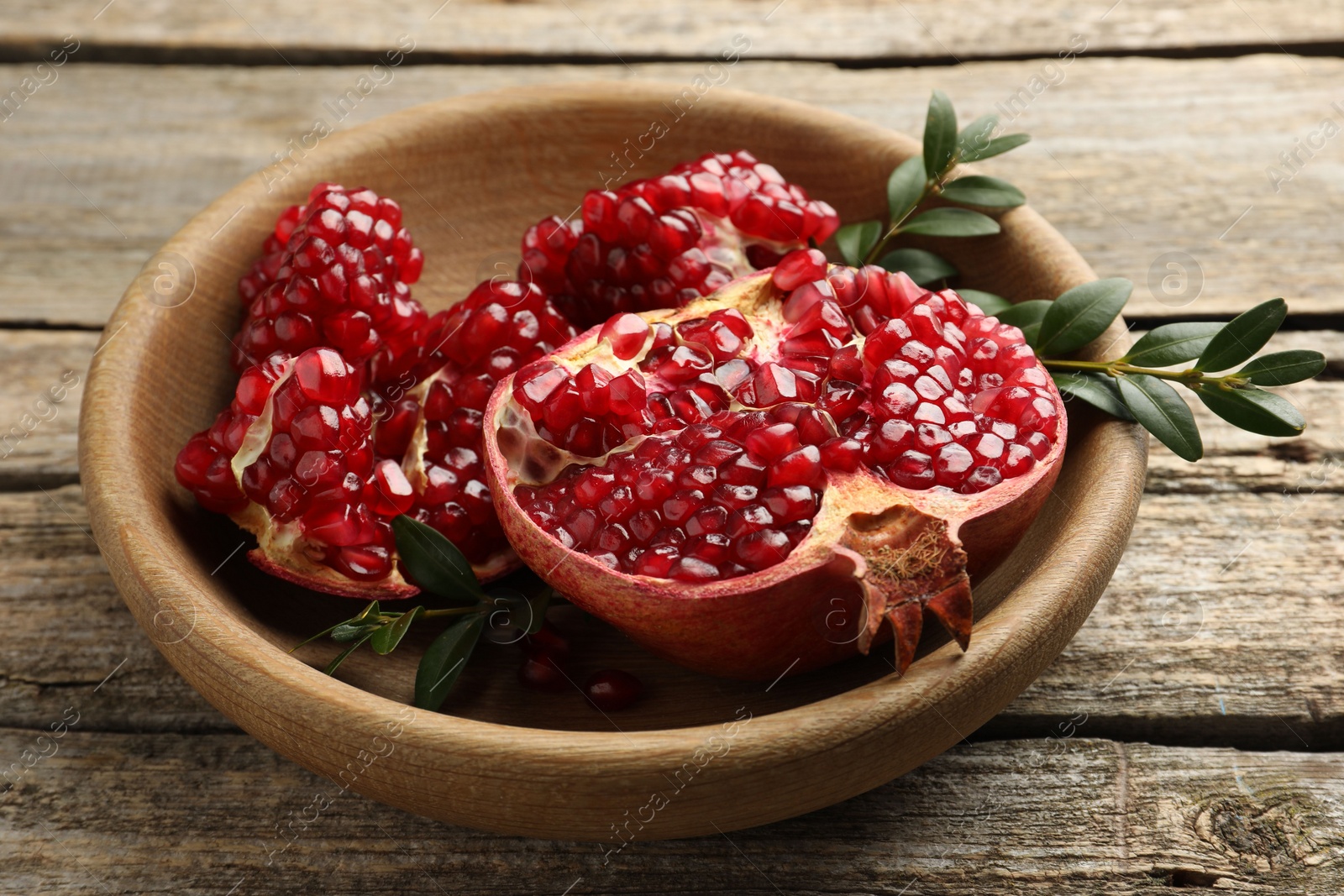 Photo of Cut fresh pomegranate and green leaves on wooden table, closeup