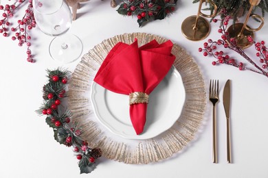 Photo of Plates with red fabric napkin, cutlery and festive decor on white table, flat lay