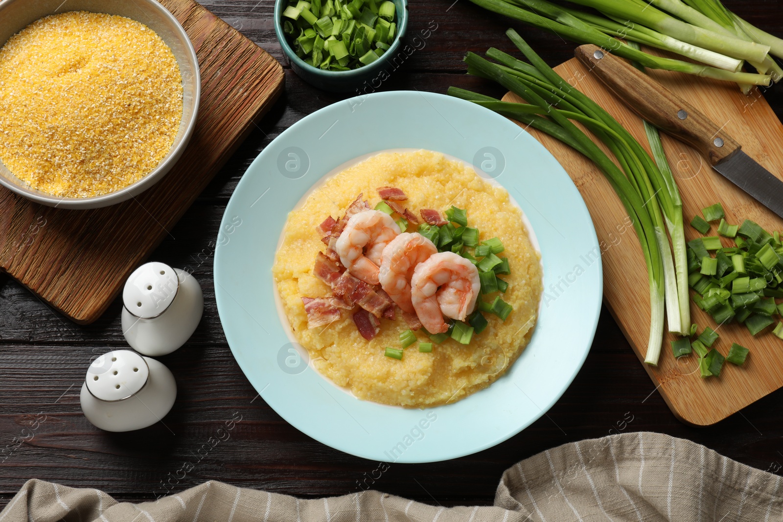Photo of Plate with fresh tasty shrimps, bacon, grits and green onion on dark wooden table, flat lay