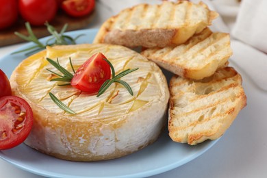 Photo of Tasty baked brie cheese with rosemary, cherry tomatoes and bread on white table, closeup