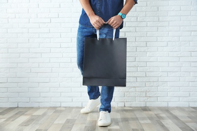 Young man holding paper bag against brick wall, closeup.  Mockup for design