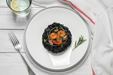 Photo of Delicious black risotto with seafood served on white wooden table, flat lay