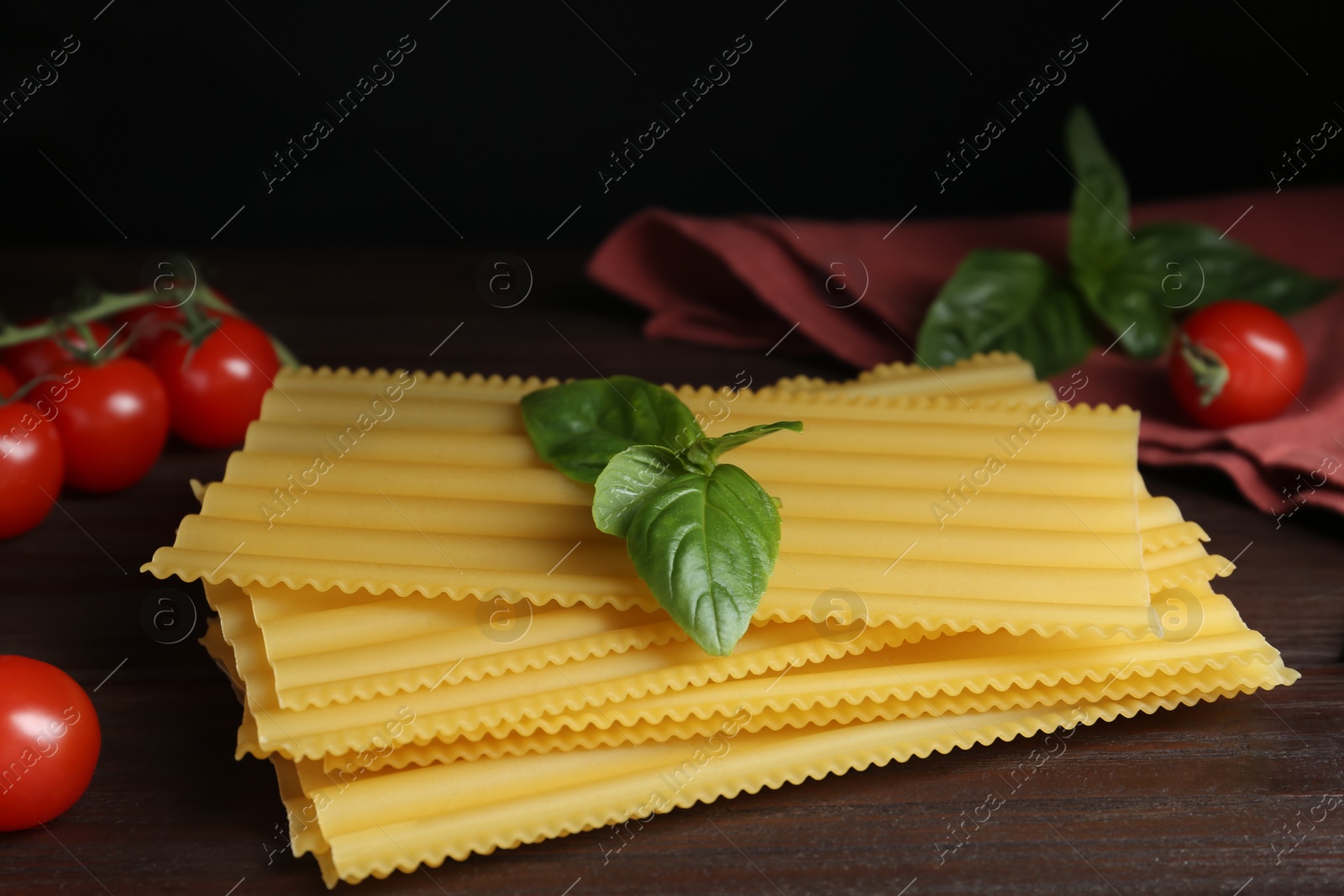 Photo of Uncooked lasagna sheets with cherry tomatoes and basil on wooden table
