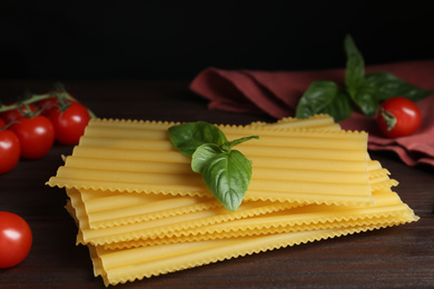 Photo of Uncooked lasagna sheets with cherry tomatoes and basil on wooden table