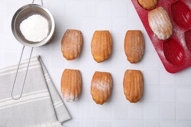 Photo of Delicious madeleine cookies, sieve with powdered sugar and baking mold on white tiled table, flat lay