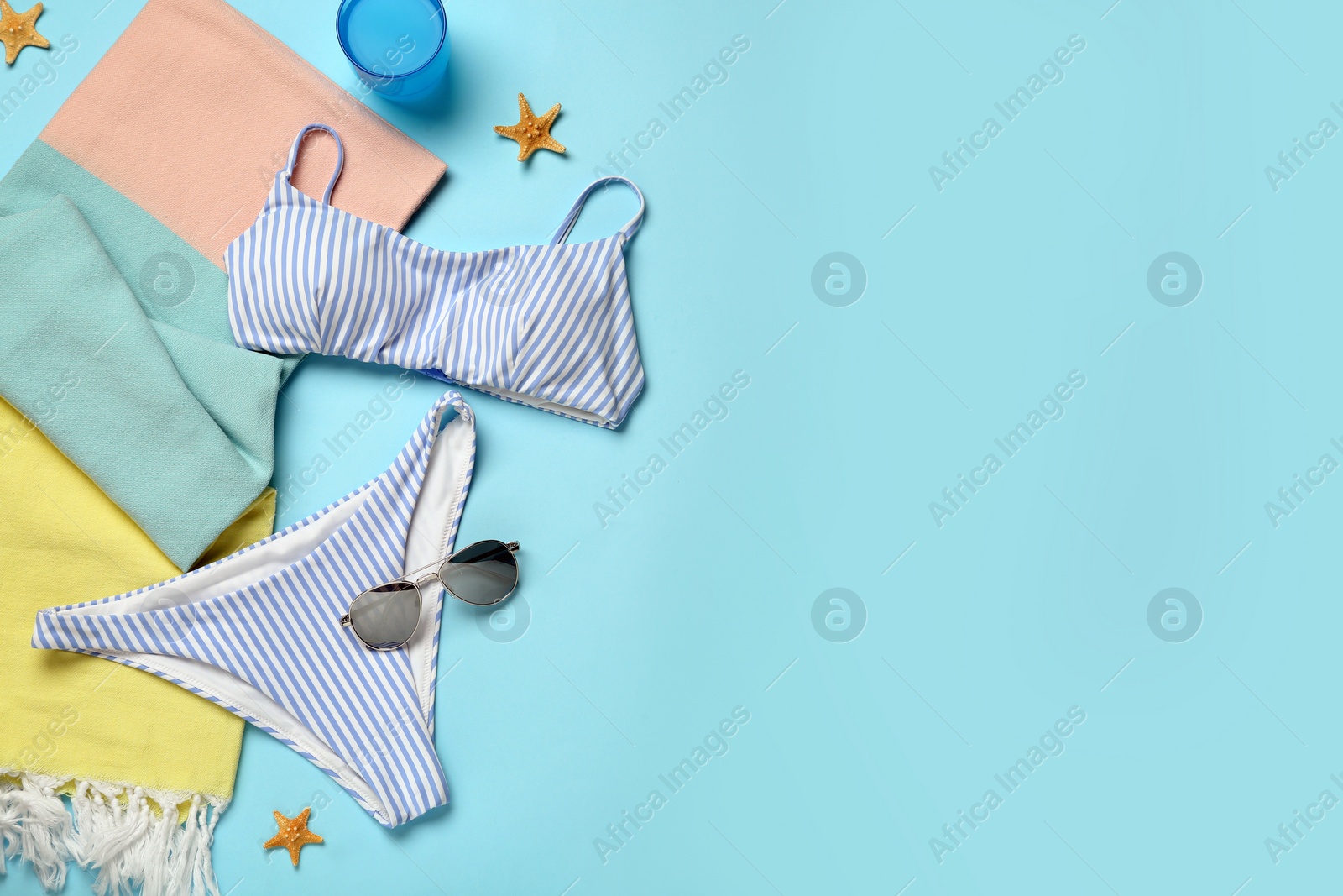 Photo of Beach towel, swimsuit and sunglasses on light blue background, flat lay. Space for text