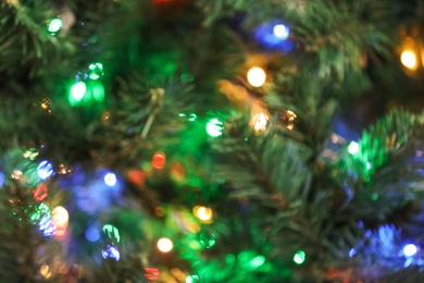 Blurred view of Christmas tree with bright string lights, closeup. Bokeh effect