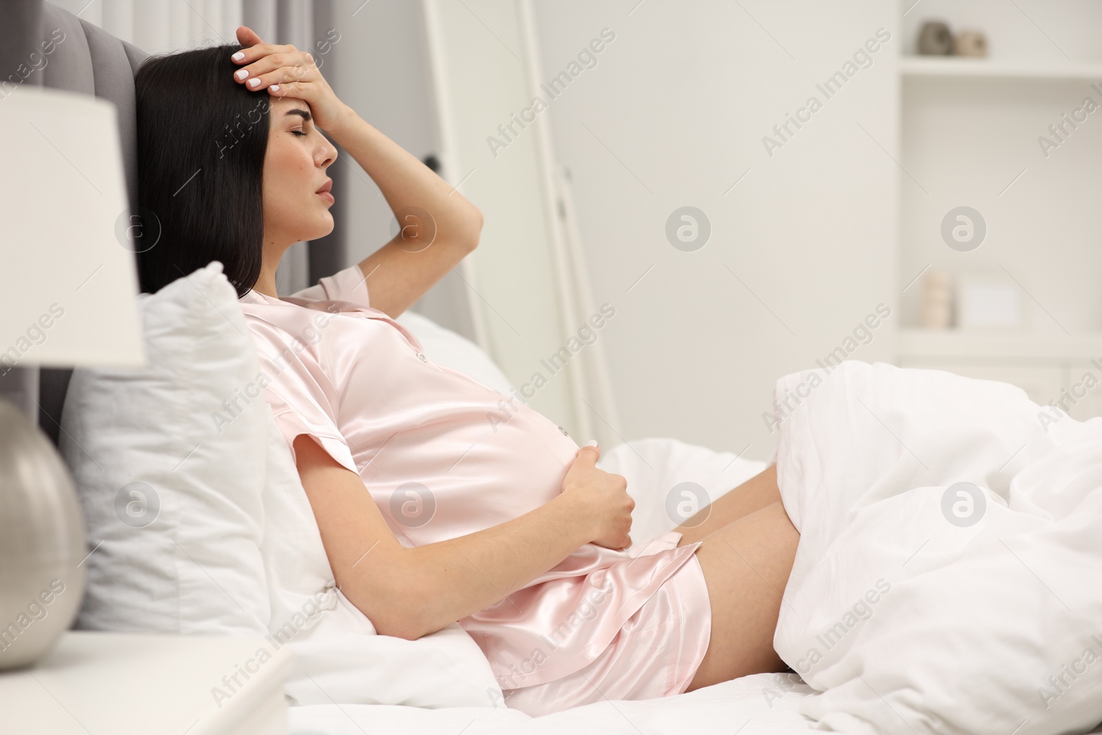 Photo of Pregnant woman suffering from headache on bed at home