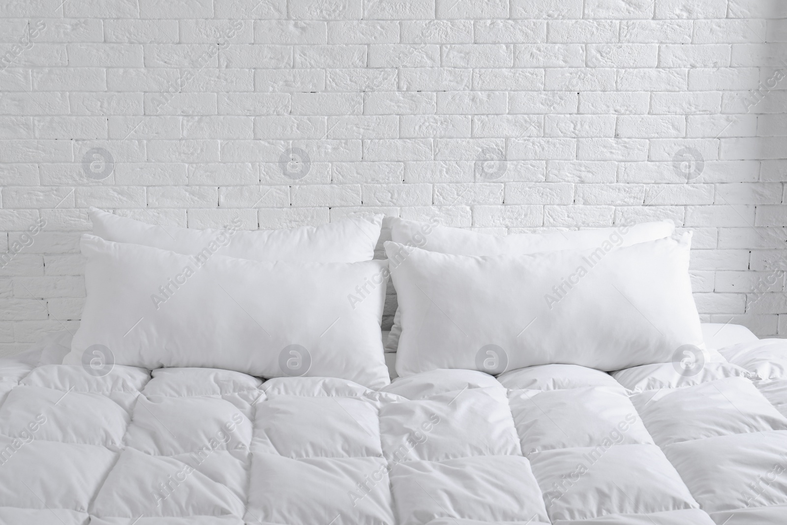 Photo of Large comfortable bed with pillows and blanket near white brick wall indoors. Stylish interior