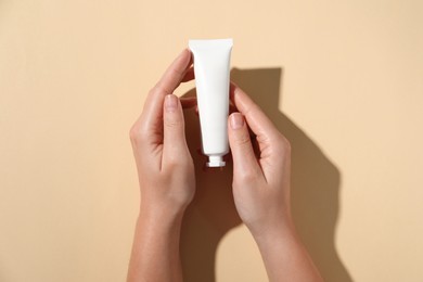 Photo of Woman with tube of hand cream on beige background, top view