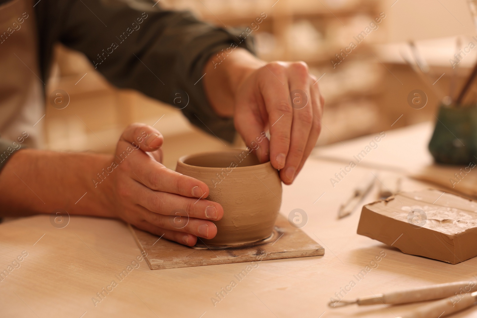Photo of Clay crafting. Man making bowl at table indoors, closeup