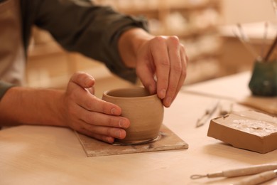 Photo of Clay crafting. Man making bowl at table indoors, closeup