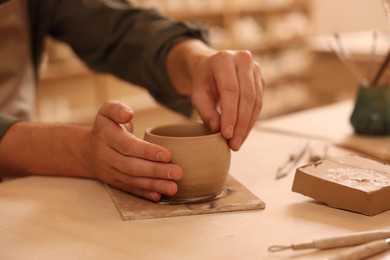 Clay crafting. Man making bowl at table indoors, closeup