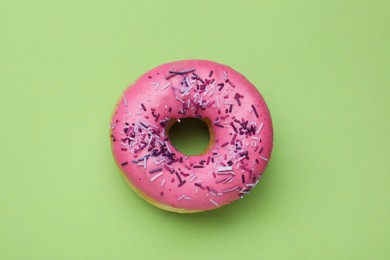 Photo of Glazed donut decorated with sprinkles on green background, top view. Tasty confectionery