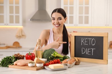 Happy woman holding chalkboard with words Keto Diet near different products in kitchen