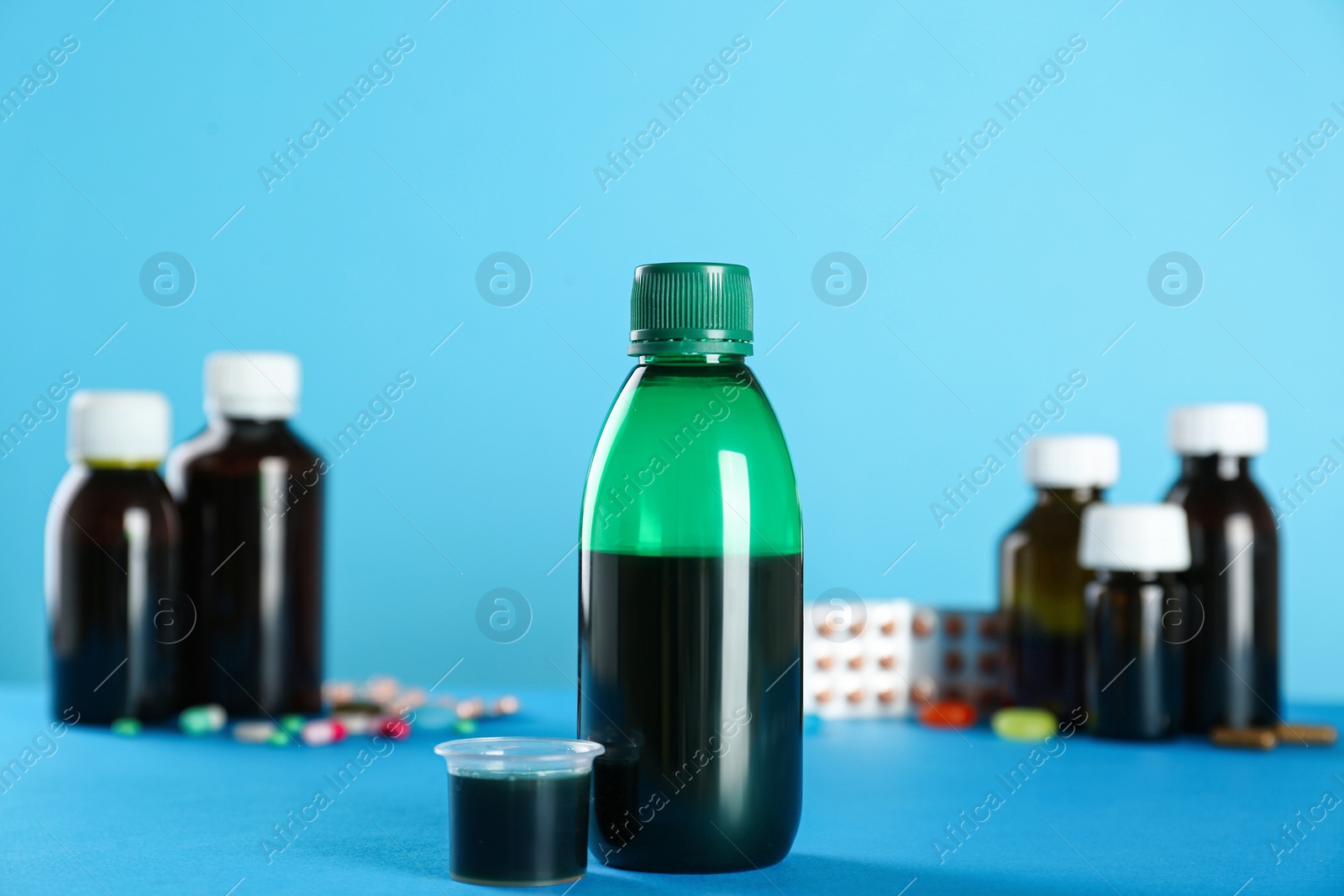 Photo of Bottle of cough syrup and measuring cup on light blue background