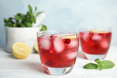 Photo of Tasty refreshing cranberry cocktail with lemon on white wooden table, closeup