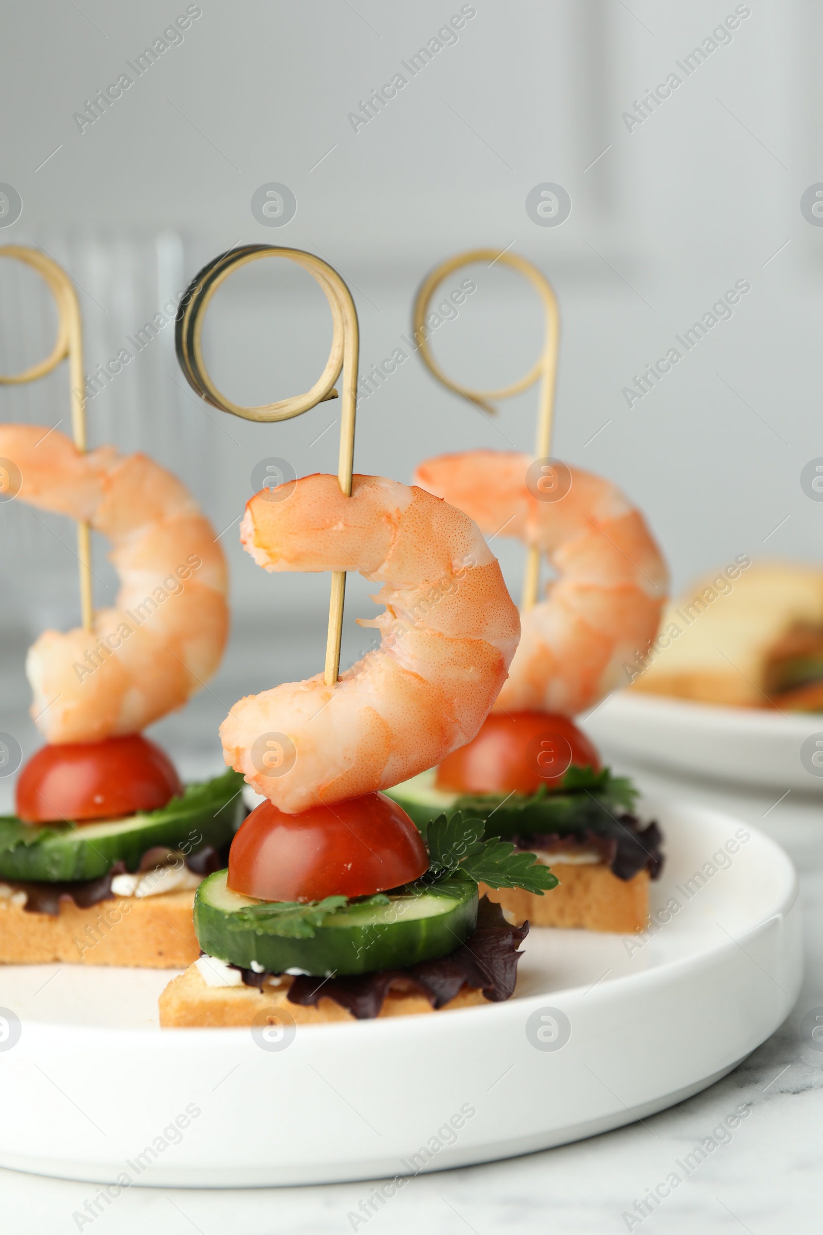 Photo of Tasty canapes with shrimps, cucumber, greens and tomatoes on white marble table, closeup