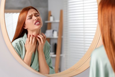 Suffering from allergy. Young woman scratching her neck near mirror in bathroom