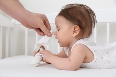Photo of Father wiping runny nose of little baby with napkin on bed, closeup