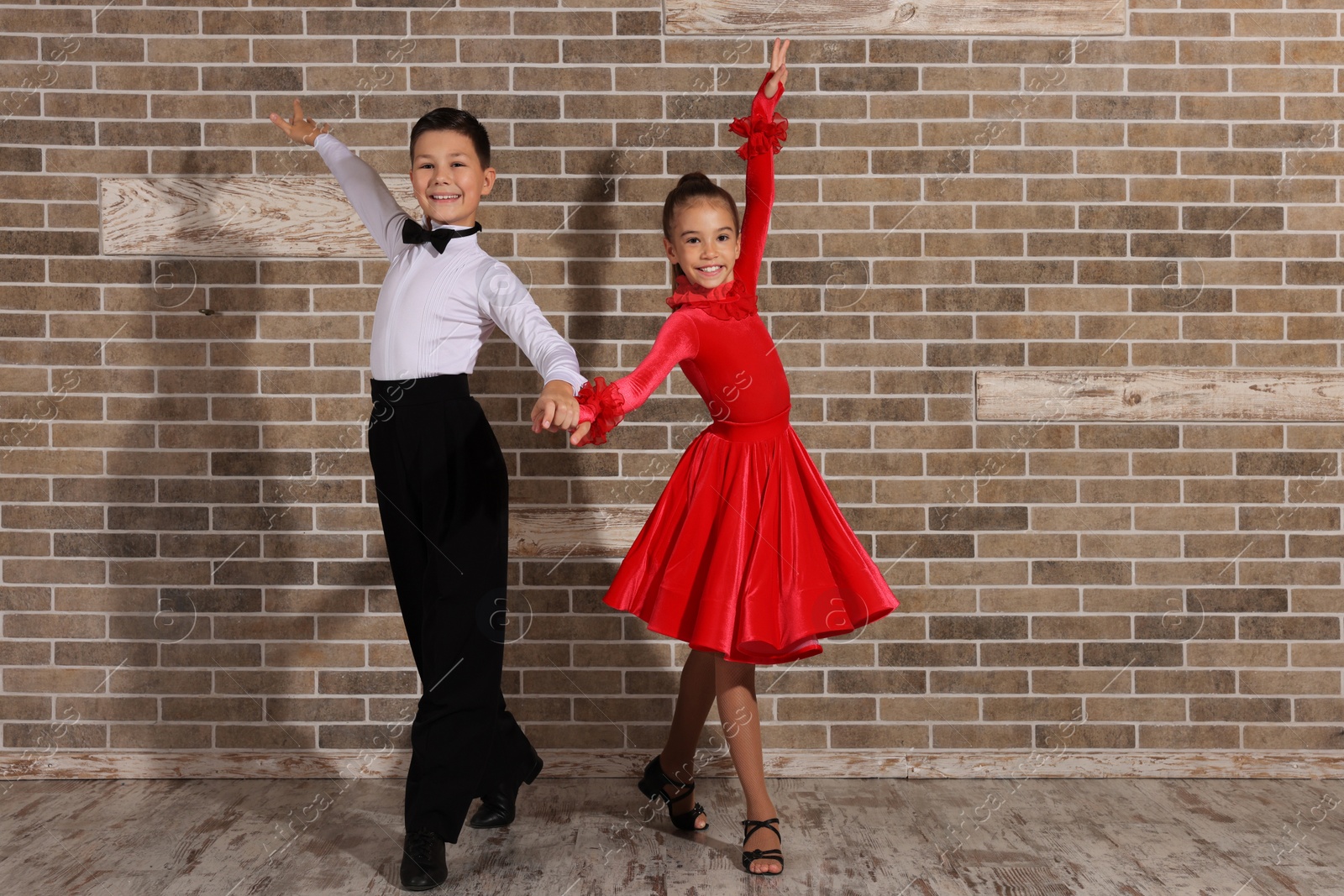 Photo of Beautifully dressed couple of kids dancing together near brick wall indoors