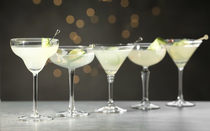 Glasses of martini with cucumber on grey table against blurred lights
