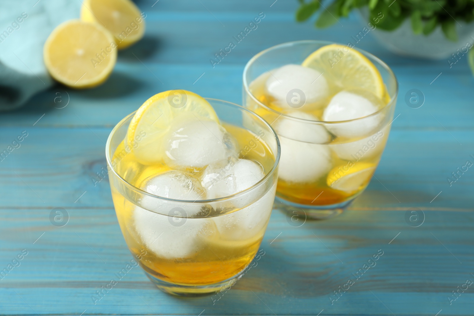 Photo of Delicious cocktails with lemon and ice balls on light blue wooden table