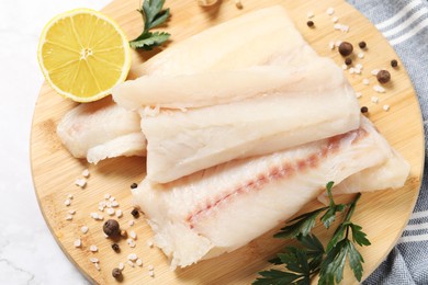 Photo of Pieces of raw cod fish, spices, parsley and lemon on white marble table