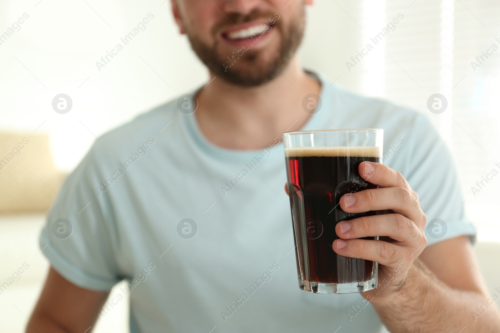 Photo of Young man with cold kvass indoors, closeup. Traditional Russian summer drink