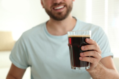 Young man with cold kvass indoors, closeup. Traditional Russian summer drink