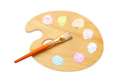 Photo of Wooden artist's palette with samples of pastel paints and brush isolated on white, top view