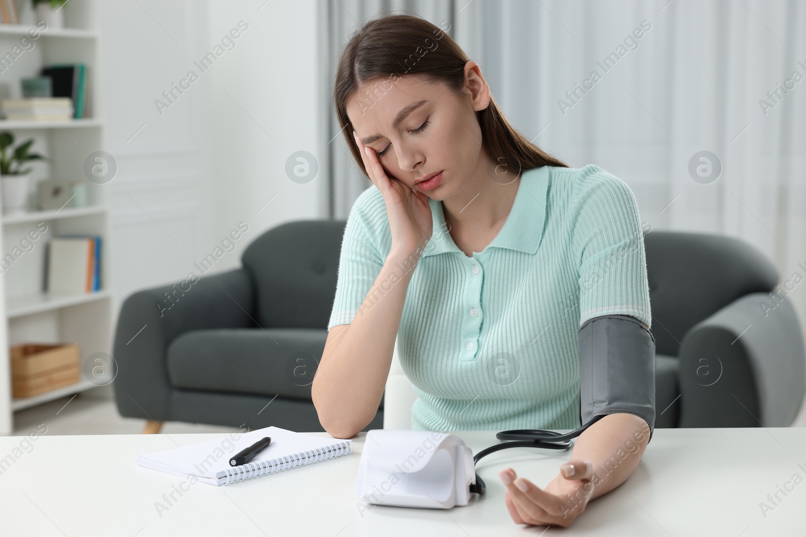 Photo of Woman suffering from headache and measuring blood pressure with tonometer at home