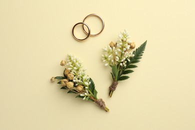 Small stylish boutonnieres and rings on beige background, flat lay