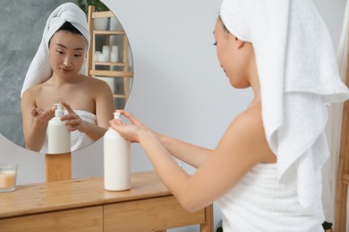 Photo of Beautiful young Asian woman applying body cream on hands in bathroom