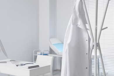 Photo of White doctor's gown hanging on rack in clinic. Space for text