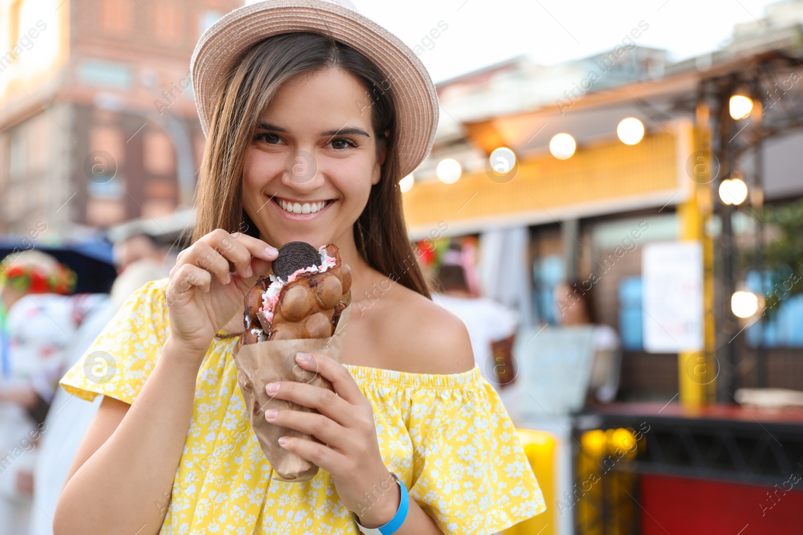 Photo of Pretty young woman holding delicious sweet bubble waffle with ice cream outdoors