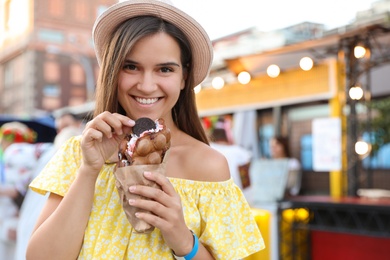 Pretty young woman holding delicious sweet bubble waffle with ice cream outdoors